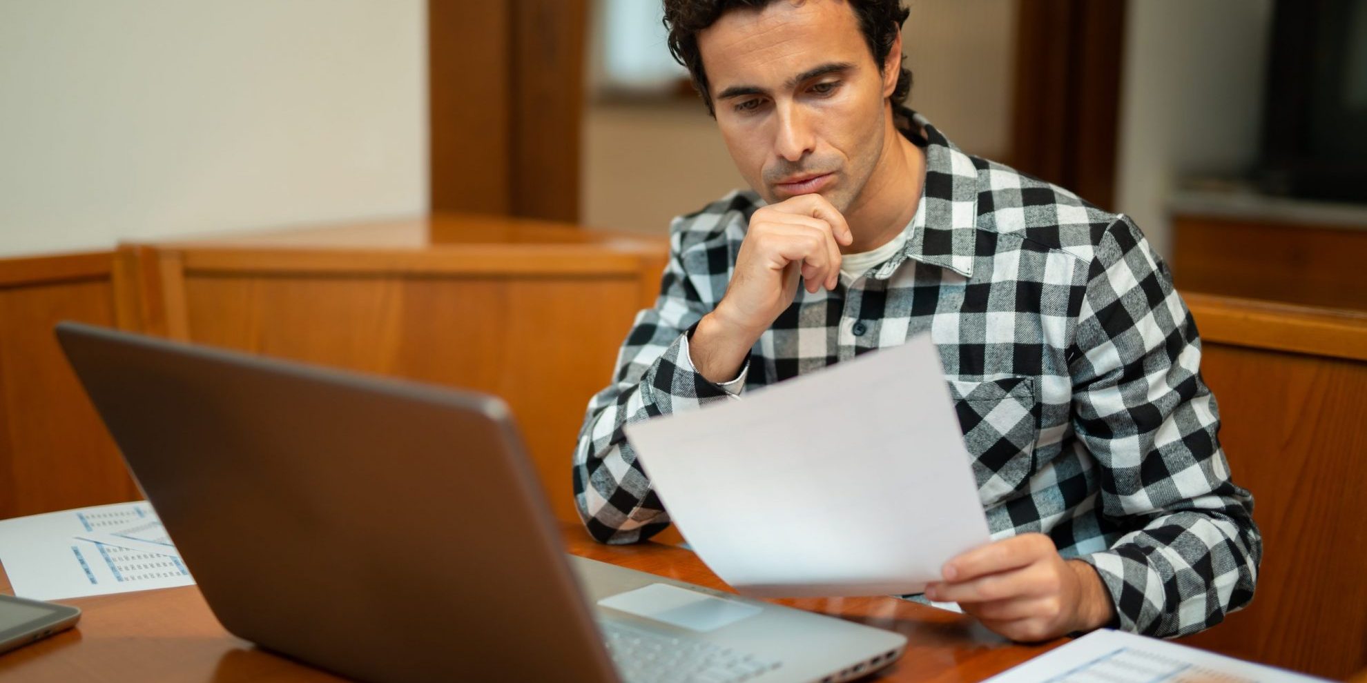 Foto de hombre leyendo papeles frente a una computadora ilustra blog: "¿Qué países tienen TPS, Estatus de Protección Temporal?"
