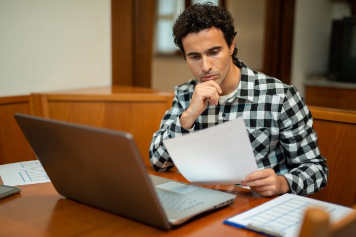 Foto de hombre leyendo papeles frente a una computadora ilustra blog: "¿Qué países tienen TPS, Estatus de Protección Temporal?"